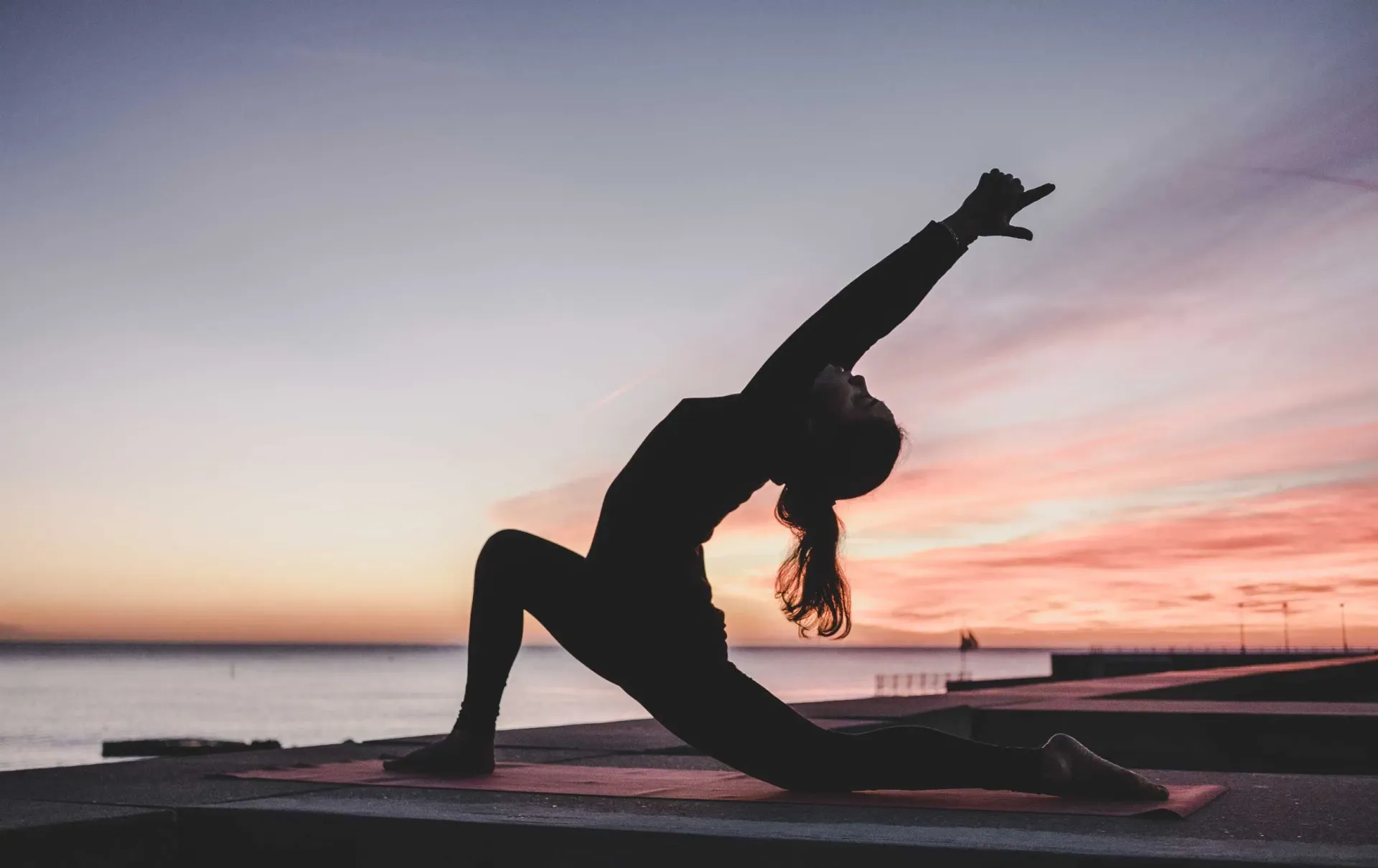 Woman practicing yoga in silhouette at sunset by the ocean